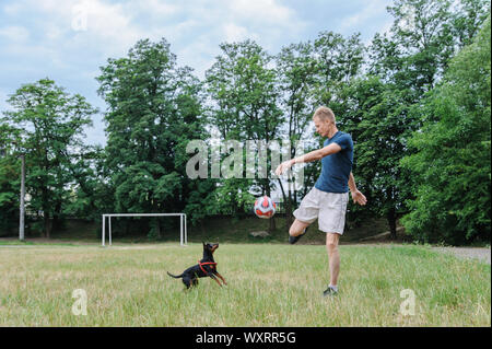 L'uomo con un cane sta giocando con un pallone da calcio. Foto Stock