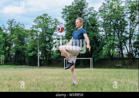 Gioco di calcio. L'uomo è calci palla calcio dal ginocchio. Foto Stock