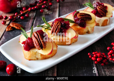 Antipasti Crostini con mele, Cranberries, Brie e le noci pecan. Chiudere su un piatto di portata contro uno sfondo di legno. Foto Stock