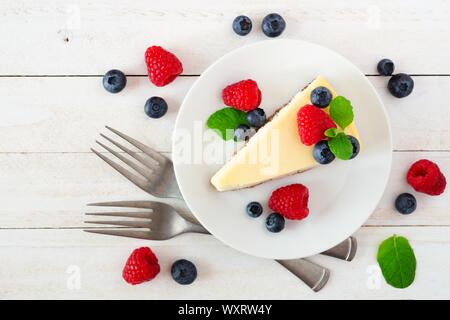 Fetta di cheesecake con mirtilli e lamponi, vista dall'alto sulla scena di un luminoso, bianco sullo sfondo di legno Foto Stock