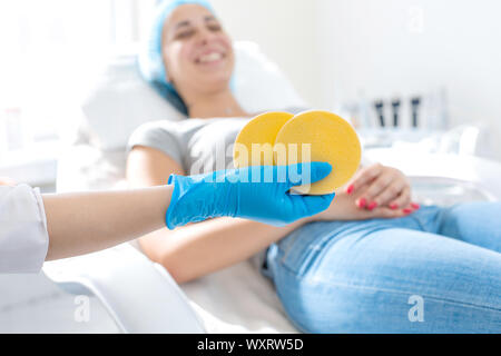 La mano del parrucchiere detiene il massaggio pastiglia contro lo sfondo di un felice paziente. Foto Stock