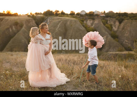 Elegante ragazzo dà un grande fiore a sua madre in un campo al tramonto. Foto Stock