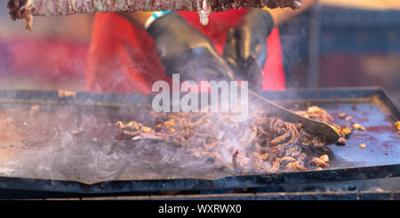 Lo Chef il taglio di carne a fette da un Döner Kebab tostatura su un girarrosto con un coltello di grandi dimensioni in un vassoio di metallo al di sotto di Foto Stock