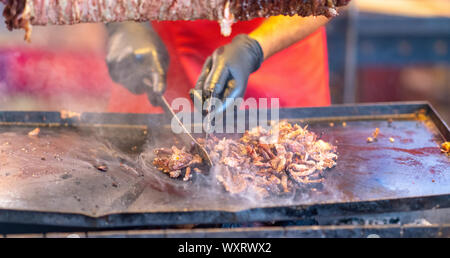 Lo Chef girando un mucchio di carne scolpita da un Döner Kebab con una spatola su un vassoio riscaldato nel corso di un incendio in un mercato di strada o un evento Foto Stock