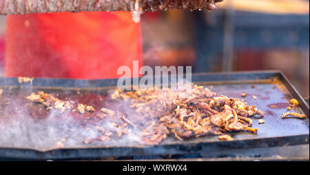 Trucioli di carne piccante intagliato fuori un Döner Kebab grigliare su una rotisserie sopra giacente in un metallo riscaldato il vassoio su un fuoco Foto Stock