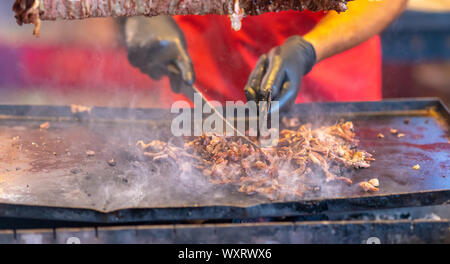 Lo Chef carving Condite la carne piccante da un Döner Kebab in un vassoio riscaldato sotto a un mercato di strada o catering eventi in una stretta fino alle mani Foto Stock