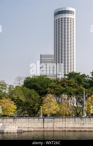 Singapore - Marzo 21, 2019: dal Fiume Singapore. Il grattacielo alto noto come Swissotel The Stamford dietro verde dal parco Esplanade sotto luce blu Foto Stock