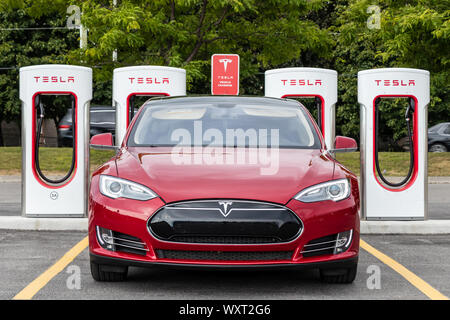 Davanti a Tesla Model S parcheggiata presso la stazione Tesla Supercharger con dietro una strada trafficata. Foto Stock