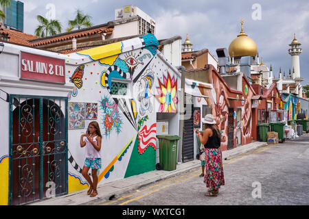 I turisti in un colorato back lane decorate con pitture murali in Kampong Glam zona, Singapore, con il punto di riferimento la Moschea del Sultano in background Foto Stock