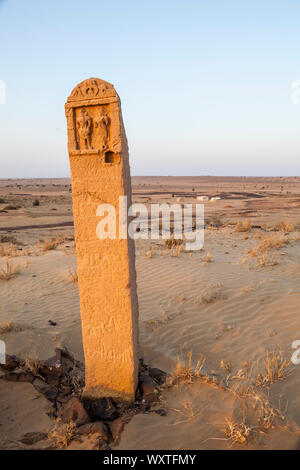 Un marcatore di pietra su una collina di sabbia al di sopra di un campo che è parte di un turista trekking cammello nel deserto del Thar del Rajasthan, India. Foto Stock