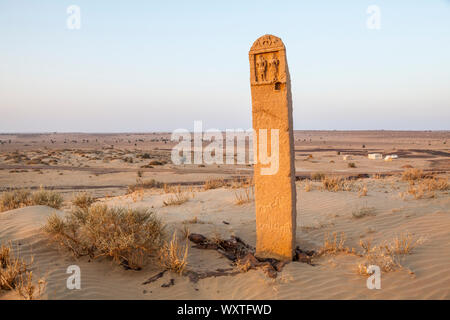 Un marcatore di pietra su una collina di sabbia al di sopra di un campo che è parte di un turista trekking cammello nel deserto del Thar del Rajasthan, India. Foto Stock