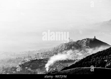 Una vista da sopra della città di Assisi (Umbria, Italia) nel mezzo della nebbia, con fumo in primo piano Foto Stock