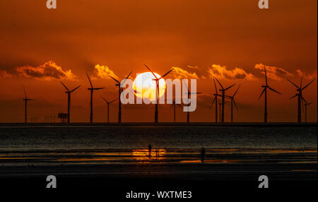 Il sole tramonta dietro Burbo Bank wind farm e 'un altro luogo", un arte di installazione da Anthony Gormley, a Crosby Beach in Merseyside nel nord ovest dell'Inghilterra. Foto Stock