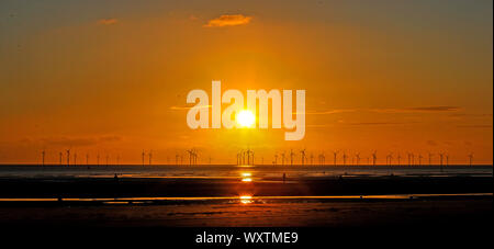 Il sole tramonta dietro Burbo Bank wind farm e 'un altro luogo", un arte di installazione da Anthony Gormley, a Crosby Beach in Merseyside nel nord ovest dell'Inghilterra. Foto Stock