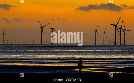 Il sole tramonta dietro Burbo Bank wind farm e 'un altro luogo", un arte di installazione da Anthony Gormley, a Crosby Beach in Merseyside nel nord ovest dell'Inghilterra. Foto Stock