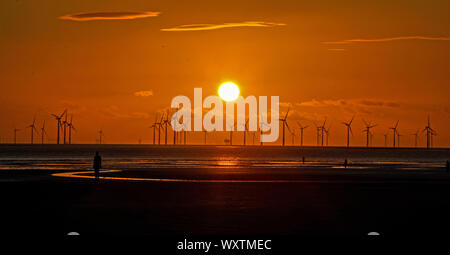 Il sole tramonta dietro Burbo Bank wind farm e 'un altro luogo", un arte di installazione da Anthony Gormley, a Crosby Beach in Merseyside nel nord ovest dell'Inghilterra. Foto Stock