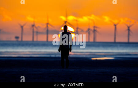 Il sole tramonta dietro Burbo Bank wind farm e 'un altro luogo", un arte di installazione da Anthony Gormley, a Crosby Beach in Merseyside nel nord ovest dell'Inghilterra. Foto Stock