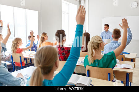 Istruzione, apprendimento e concetto di persone - insegnante maschio e un gruppo di studenti di scuola superiore alzando le mani in aula Foto Stock