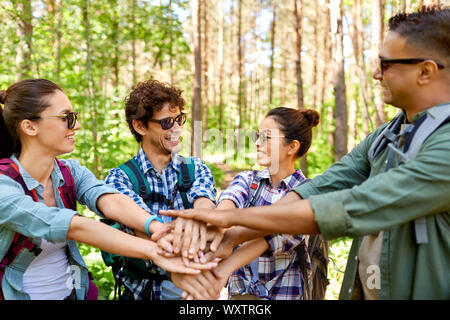 Turismo, viaggio, escursione e il concetto di amicizia - gruppo di amici con zaini mani di impilamento in foresta Foto Stock