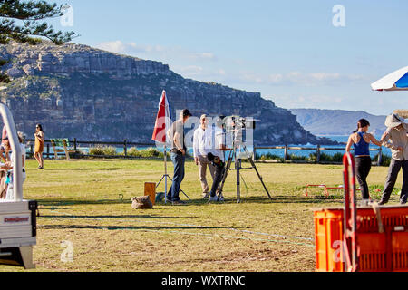 Attori e troupe tra cui un operatore della telecamera in attesa di film una scena esterna di Home & Away programma televisivo a Palm Beach, NSW, Australia Foto Stock