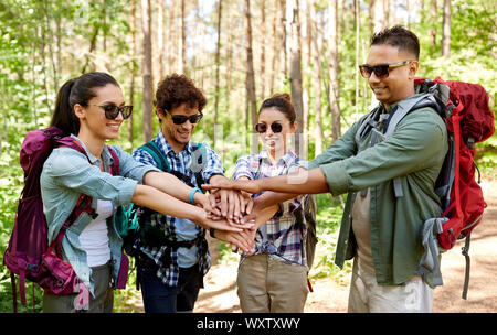 Turismo, viaggio, escursione e il concetto di amicizia - gruppo di amici con zaini mani di impilamento in foresta Foto Stock