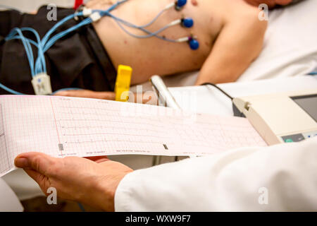 Il cardiologo holding e rivedere l'elettrocardiografo ECG o ECG diagramma stampato su carta a griglia. Foto Stock