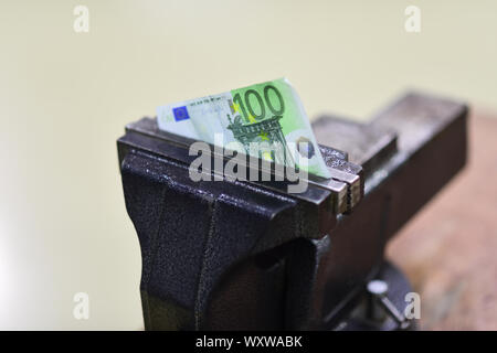 Centinaia di banconote in euro schiacciato in una morsa. Attrezzo morsa per fissare la carta moneta su un banco di lavoro. Euro la svalutazione della moneta o di inflazione e di default. Finanza e bankin Foto Stock