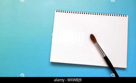 Vuoto bianco sketch pad con un grande acqua spazzola di colore, su una vivace sfondo blu. Foto Stock