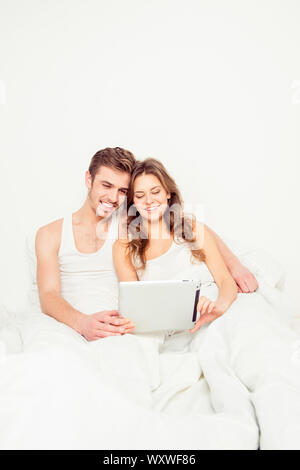 Coppia felice in amore seduta a letto e guardando nel tablet Foto Stock