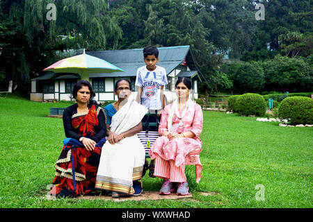 Due giovani e un anziano signora seduta su una panchina di lady hydari park con un ragazzo, capretto, in background una teglia coperta e casa molto bella e verde gla Foto Stock