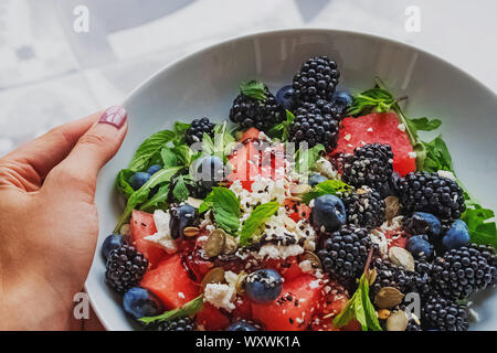 Donna di mano che tiene una piastra con una deliziosa insalata con cocomero, rucola, frutti di bosco e aceto balsamico condimento Foto Stock