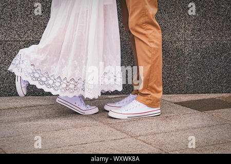 Close-up shot dell uomo e della donna in piedi lo stesso sneakers in piedi di fronte ad ogni altro. Passeggiata romantica o di incontri in città. Foto Stock