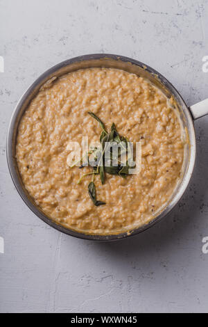 Risotto alla zucca con parmigiano e salvia serviti con un bicchiere di vino bianco. Vista aerea, sullo sfondo di calcestruzzo Foto Stock