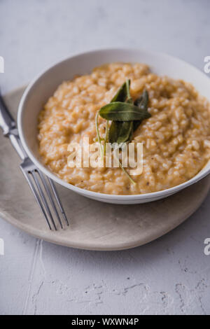 Risotto alla zucca con parmigiano e salvia serviti con un bicchiere di vino bianco. Vista laterale, sullo sfondo di calcestruzzo Foto Stock