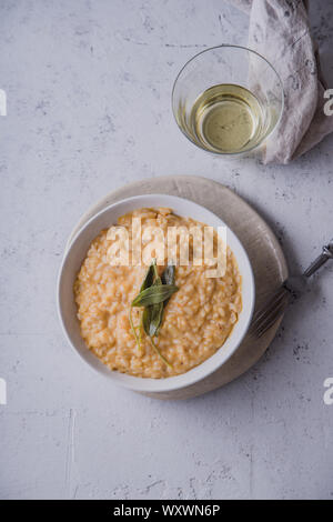 Risotto alla zucca con parmigiano e salvia serviti con un bicchiere di vino bianco. Vista aerea, sullo sfondo di calcestruzzo Foto Stock