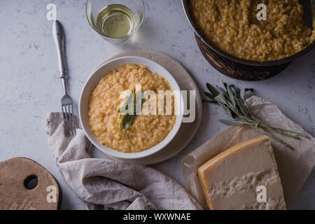 Risotto alla zucca con parmigiano e salvia serviti con un bicchiere di vino bianco. Vista aerea, sullo sfondo di calcestruzzo Foto Stock