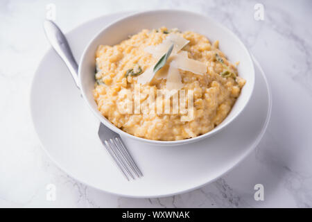 Risotto alla zucca con parmigiano e salvia. Marmo bianco sullo sfondo Foto Stock