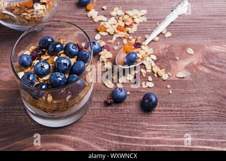 Yogurt, muesli e mirtilli in un bicchiere sul tavolo di legno. Sana colazione close-up Foto Stock