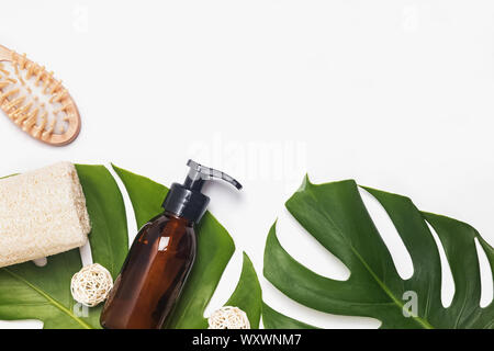 Moderno bagno eco essentials. Erogatore riutilizzabile, in legno spazzola per capelli e spugna naturale giacenti su foglie di monstera Foto Stock