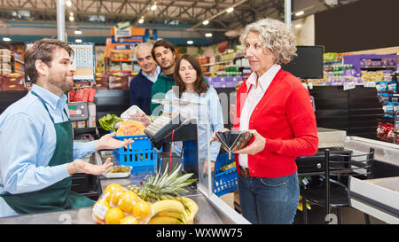 Vecchia donna è alla ricerca di denaro per pagare in portafoglio al momento del checkout dal supermercato Foto Stock