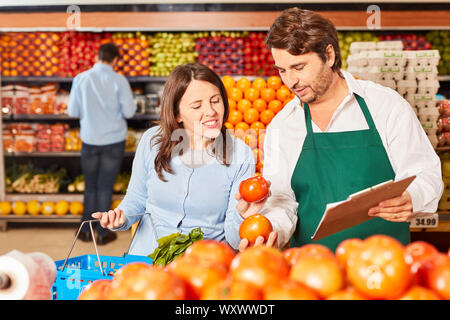 Venditore nel dipartimento di vegetali al supermercato mostra il cliente bio pomodori Foto Stock