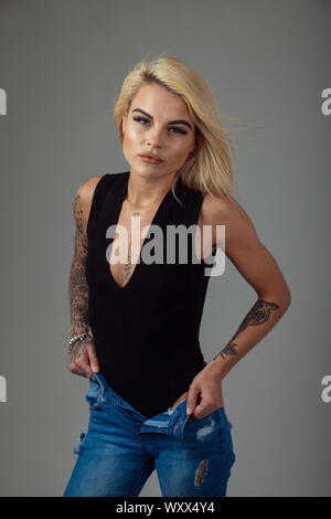 Una giovane e bella donna con tatuaggi indossando un body senza maniche e jeans strappati Foto Stock