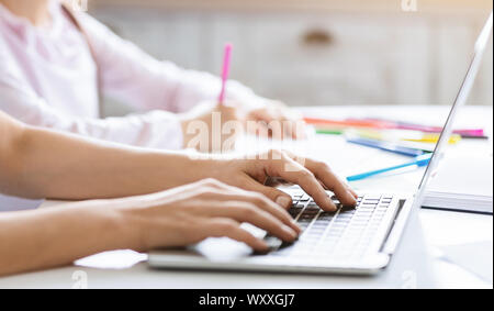Donna digitando sulla tastiera portatile mentre la figlia a fare i compiti di scuola Foto Stock