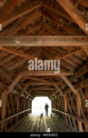 A capriate e travi in forme geometriche e uomo a camminare i cani presso il vecchio ponte coperto, ponte dalla pianura di Sheffield, Massachusetts. Foto Stock