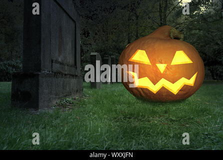 Scary grinning zucca di Halloween si trova su un cimitero Foto Stock