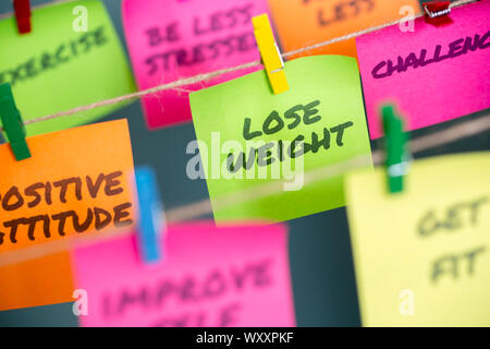 Perdere peso e altre parole motivazionale per uno stile di vita sano scritto su diversi colori sticky notes sono agganciati alle funi Foto Stock