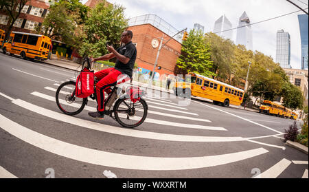 Una consegna GrubHub lavoratore, sans casco e sul suo telefono cellulare, sulla sua bicicletta elettrica nel quartiere di Chelsea di New York il giovedì, 5 settembre 2019. (© Richard B. Levine) Foto Stock