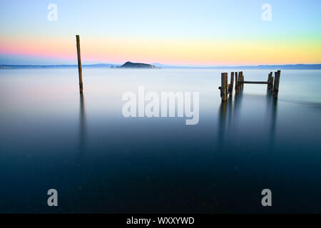 Il paesaggio del lago di Bolsena all'alba, con una lunga esposizione, colorato di sky e pali di legno in acqua con la Martana in background Foto Stock