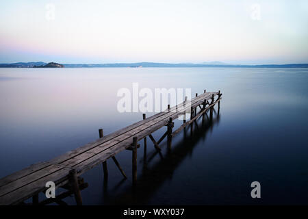 Una lunga esposizione di un paesaggio con un vecchio molo in legno sulle acque del lago di Bolsena Foto Stock