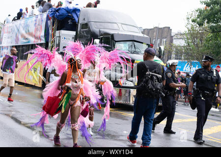 Tanzend zu lauter Musik laufen zwei Frauen mit rosafarbenem Kostüm und Federn auf der West Indian Day Parade di New York City Un den Zuschauern vorbei Foto Stock